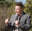 El gobernador Pablo Lemus, vistiendo un saco gris y chaleco beige, habla con determinación sosteniendo un micrófono durante un evento al aire libre.