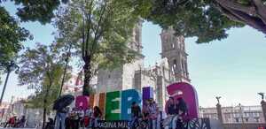 personas descansan sobre las letras de puebla en zócalo y detrás está la catedral de puebla