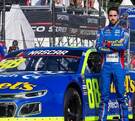 Rubén García Jr. con los brazos cruzados frente a su automóvil 88 en una competencia NASCAR