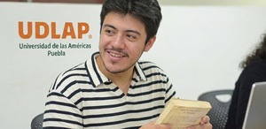 Alumno con un libro en las manos frente a una laptop con logo de la UDLAP atrás
