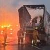Bomberos apagan el fuego en un tráiler quemado sobre una autopista.