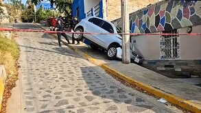 Camioneta inclinada sobre un pequeño pasillo al lado de una calle y una casa tras chocar contra un poste en una bajada acordonada por policías