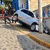 Camioneta inclinada sobre un pequeño pasillo al lado de una calle y una casa tras chocar contra un poste en una bajada acordonada por policías