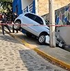 Camioneta inclinada sobre un pequeño pasillo al lado de una calle y una casa tras chocar contra un poste en una bajada acordonada por policías