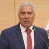 Hombre anciano vestido de traje hablando ante un micrófono.