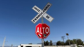 Se observa un letrero de alto en color rojo y otro que dice Cruce de Ferrocarril en color blanco.