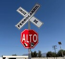 Se observa un letrero de alto en color rojo y otro que dice Cruce de Ferrocarril en color blanco.