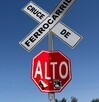 Se observa un letrero de alto en color rojo y otro que dice Cruce de Ferrocarril en color blanco.