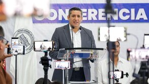 Hombre vestido de traja hablando frente a un micrófono desde la Fiscalía de Oaxaca.