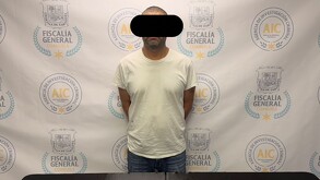 Se observa a un hombre con ojos tapados, está detenido y parado.