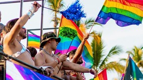 Hombres sin playera ondeando banderas de la comunidad LGBT arriba de un camión durante el Vallarta Pride en Puerto Vallarta