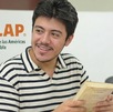 Alumno con un libro en las manos frente a una laptop con logo de la UDLAP atrás
