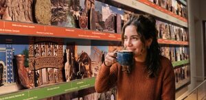 Mujer toma café con el fondo del calendario de las civilizaciones del museo Amparo en Puebla