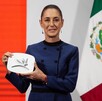 Mujer sosteniendo un objeto rectangular junto a una bandera de México.