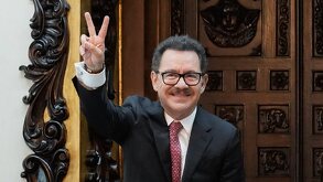 Hombre de lentes y pelo corto hace una señal con los dedos mientras sonríe.