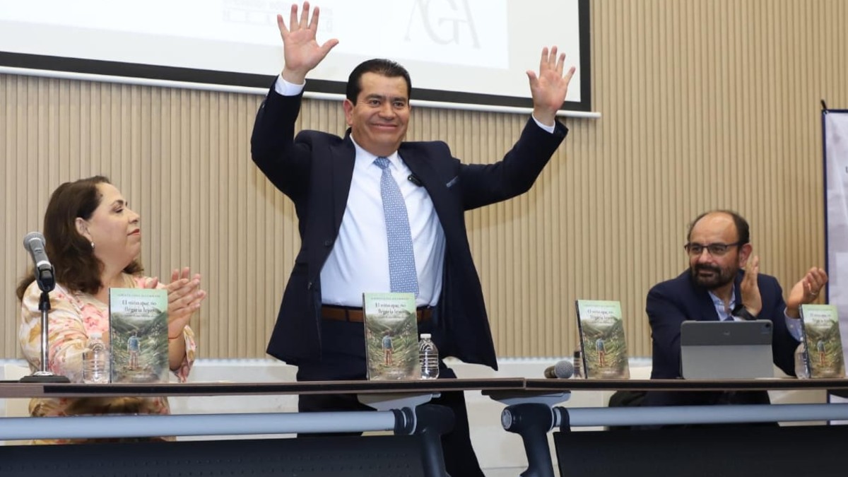 Alberto de pie frente a la mesa principal con las manos en agradecimiento después de su presentación
