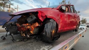 Un automóvil de color rojo destrozado de la parte delantera y en el costado derecho tras el impacto con un gran bloque de cemento.