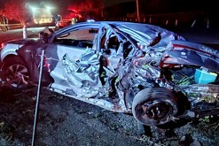 Vista lateral de un automóvil gris destruido y con los fierros retorcidos tras ser impactado por un tráiler