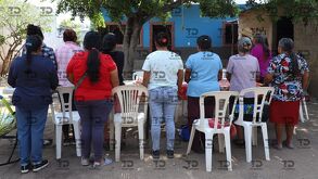 Mujeres de espaldas frente a una vivienda y mesas improvisadas.