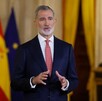 Rey de España Felipe VI hablando delante de la bandera de España y la bandera de las Naciones unidas desenfocadas en el fondo