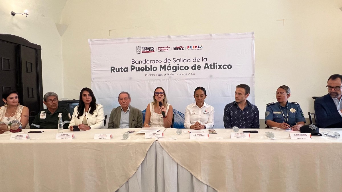 Autoridades sentadas en la mesa de diálogo, una de ellas sostiene el micrófono y de fondo el cartel de Ruta Pueblo Mágico Atlixco