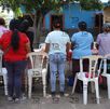 Mujeres de espaldas frente a una vivienda y mesas improvisadas.