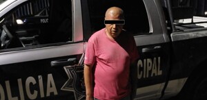 Se observa a un hombre con ojos tapados, viste una playera rojo y pantalón de mezclilla.