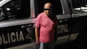 Se observa a un hombre con ojos tapados, viste una playera rojo y pantalón de mezclilla.