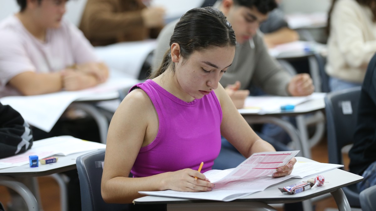 Joven aspirante a la Universidad de Guadalajara presentando el examen de admisión dentro de un salón de clases con otros aspirantes desenfocados en el fondo