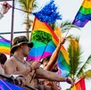 Hombres sin playera ondeando banderas de la comunidad LGBT arriba de un camión durante el Vallarta Pride en Puerto Vallarta