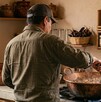 Se observa un hombre meneando un cazo de comida dentro de una cocina.