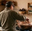 Se observa un hombre meneando un cazo de comida dentro de una cocina.