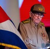 Raúl Castro con una bandera de Cuba en primer plano. El expresidente porta su unifome militar y mira en dirección hacia la bandera.