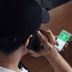 Hombre visto desde arriba vistiendo una gorra negra y sosteniendo una llamada telefónica con un celular en cada mano y un teléfono fijo al frente en una mesa