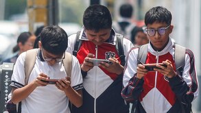 Estudiantes asisten a clases presenciales con uniformes escolares y celulares en las manos