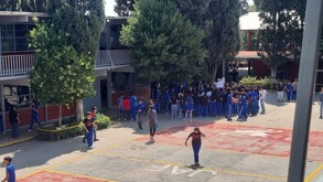 Se observa a varios jóvenes que están parados en un patio de una escuela; traen uniforme.