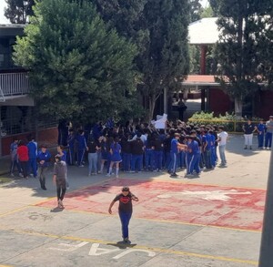 Se observa a varios jóvenes que están parados en un patio de una escuela; traen uniforme.