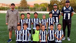 Se observa a muchos niños con uniforme en colores azul y blanco y a dos hombres a los costados.