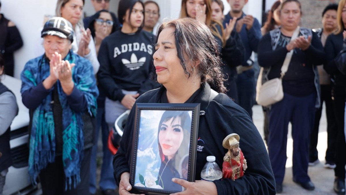 una mujer llorando sostiene una fotografía de su hija en un velorio