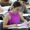 Joven aspirante a la Universidad de Guadalajara presentando el examen de admisión dentro de un salón de clases con otros aspirantes desenfocados en el fondo