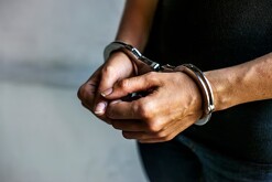 Hombre con playera negra y jeans visto del pecho hacia abajo con las manos hacia el frente y esposas colocadas