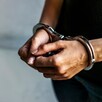 Hombre con playera negra y jeans visto del pecho hacia abajo con las manos hacia el frente y esposas colocadas