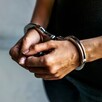 Hombre con playera negra y jeans visto del pecho hacia abajo con las manos hacia el frente y esposas colocadas
