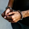 Hombre con playera negra y jeans visto del pecho hacia abajo con las manos hacia el frente y esposas colocadas