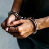 Hombre con playera negra y jeans visto del pecho hacia abajo con las manos hacia el frente y esposas colocadas