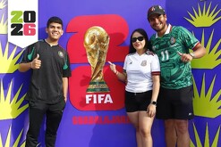 Dos hombres y una mujer delante de un cartel promocional del Fan Fest del Mundial en Guadalajara