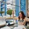 Estudiante festeja con material de estudio en su mesa y detrás las instalaciones de la BUAP