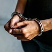 Hombre con playera negra y jeans visto del pecho hacia abajo con las manos hacia el frente y esposas colocadas