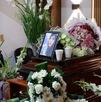 una fotografía de una mujer sobre un ataúd rodeado de flores
