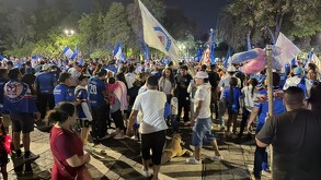 Se observa a varias personas de pie reunidas en un espacio público.